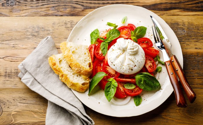 Burrata podávaná s paradajkami a lístkami bazalky.