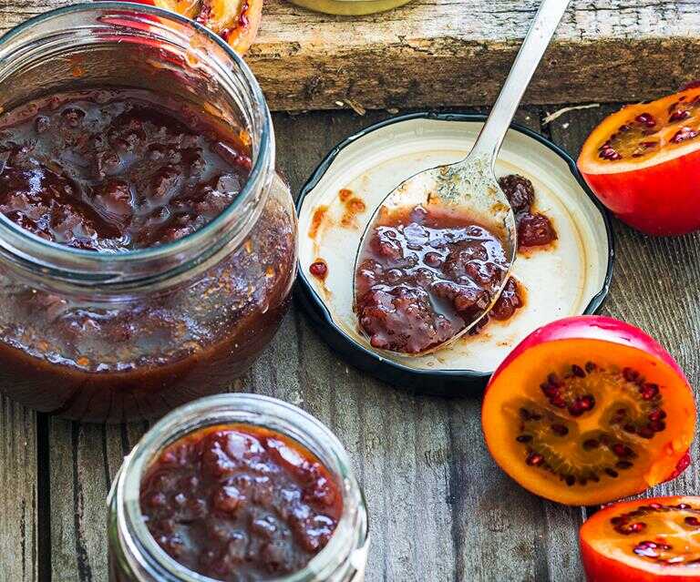 Džem z rajčiny v pohári a na lyžici s vedľa položenou čerstvou rajčinou.